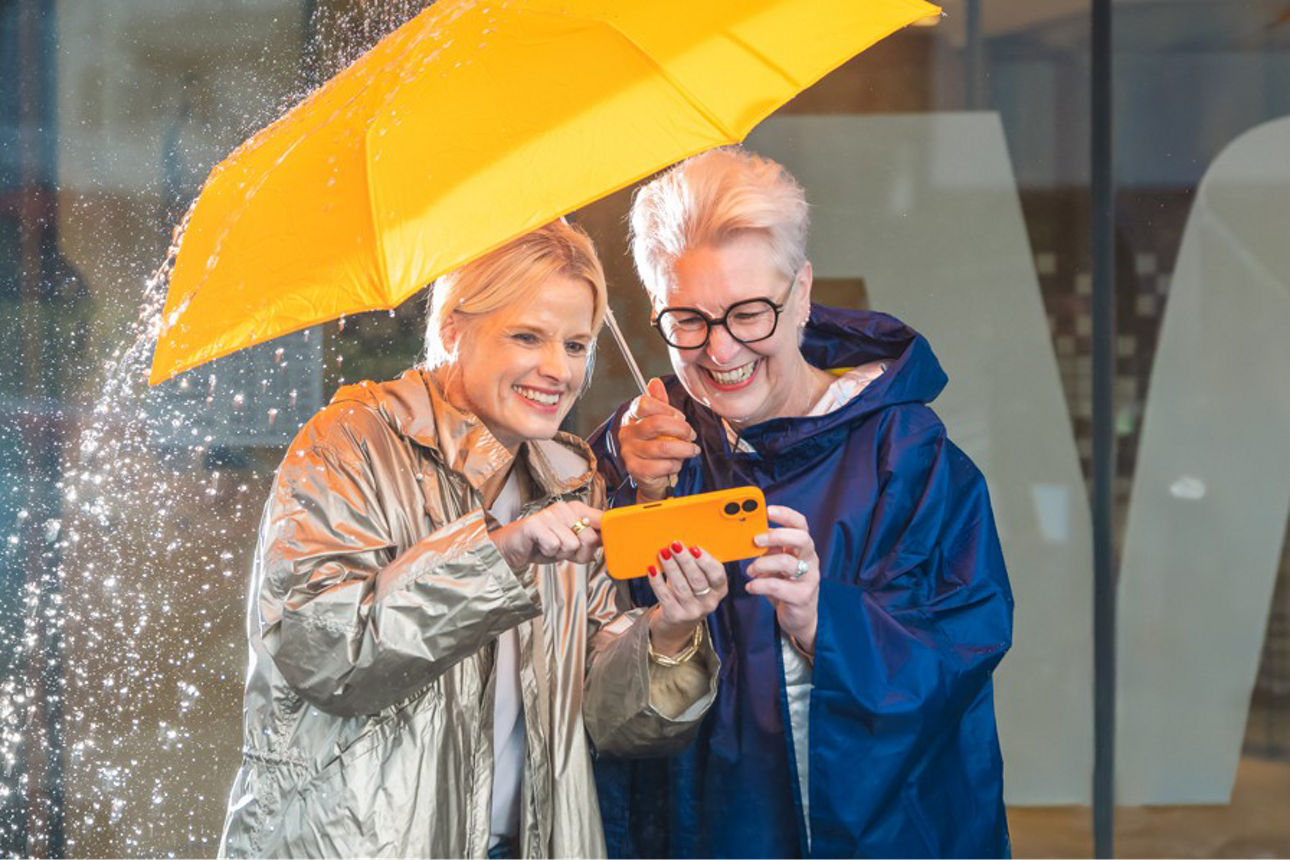 Zwei Frauen unter einem Regenschirm schauen auf ein Smartphone