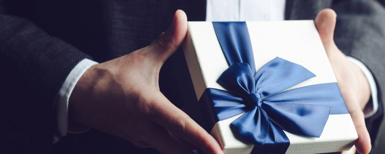 Großaufnahme von Mann im Anzug, der ein Geschenk überreicht