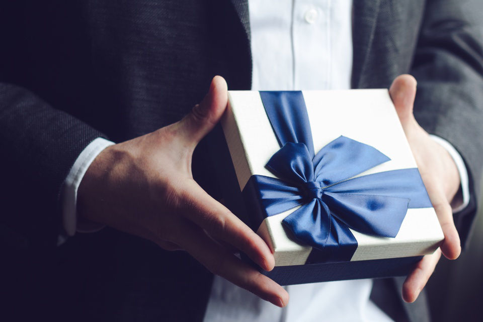 Großaufnahme von Mann im Anzug, der ein Geschenk überreicht