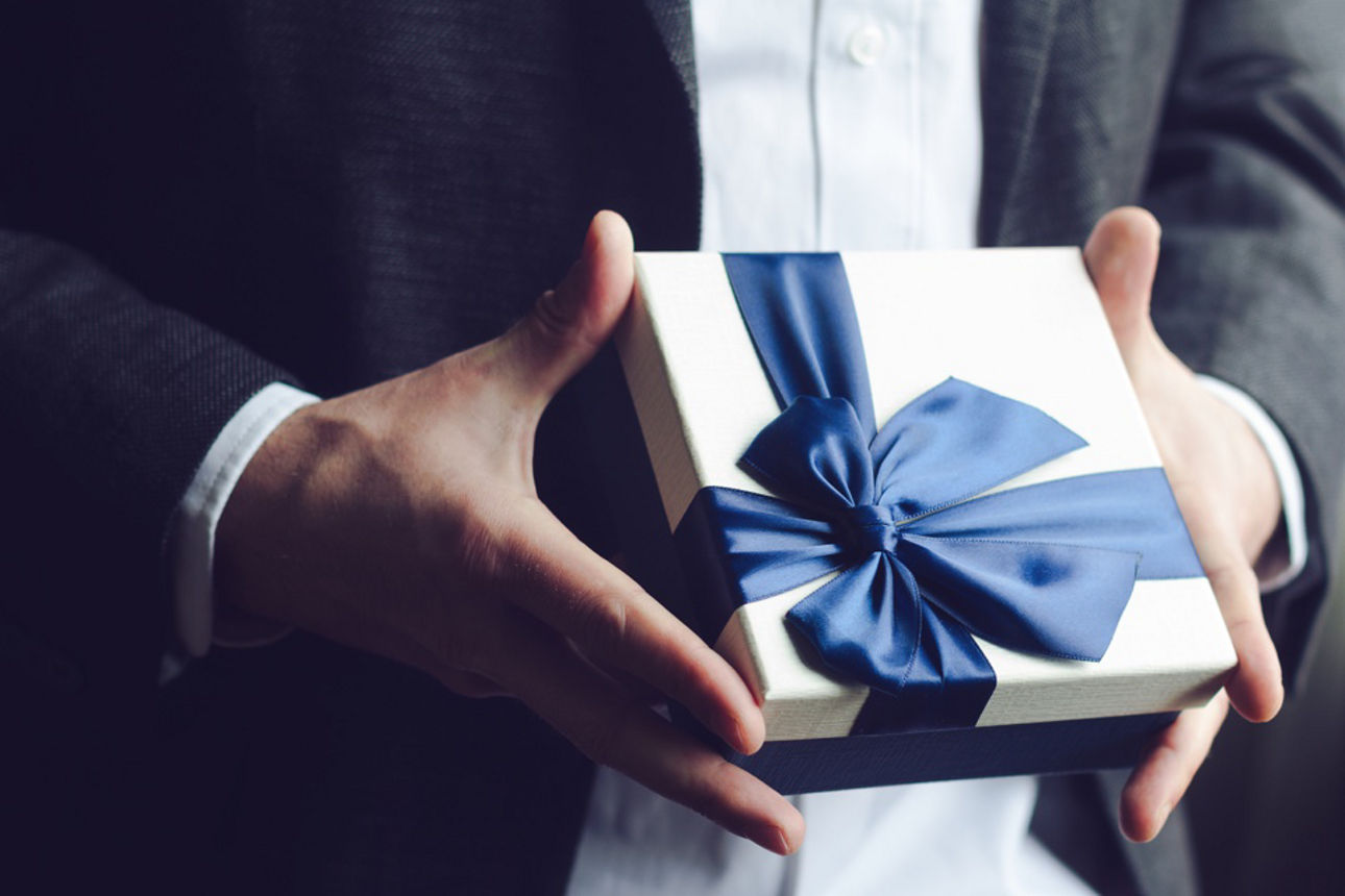 Großaufnahme von Mann im Anzug, der ein Geschenk überreicht