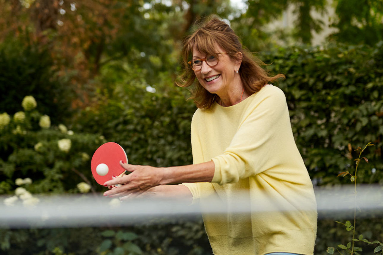 Das Bild zeigt eine Frau, die im Garten Tischtennis spielt.