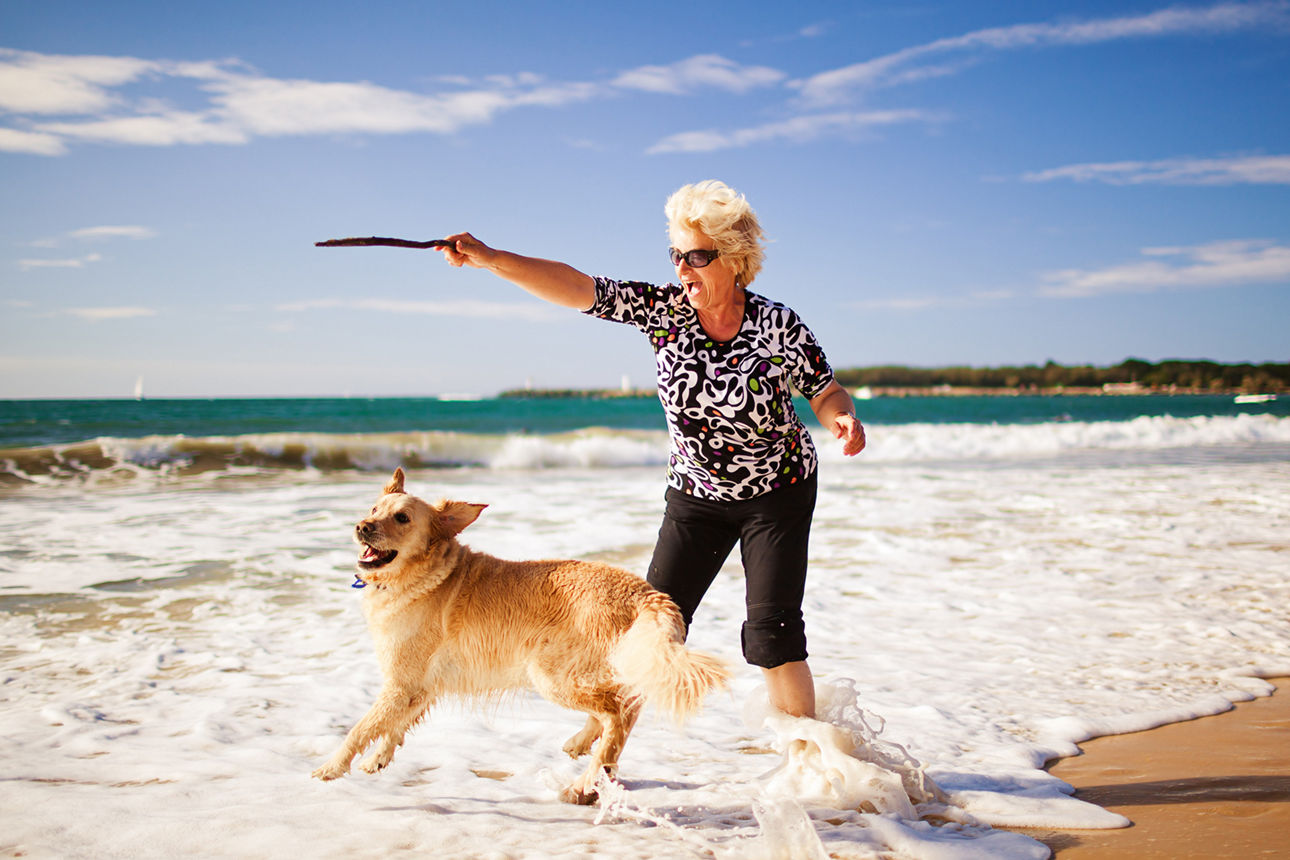 Ältere Frau mit einem Hund am Sandstrand.