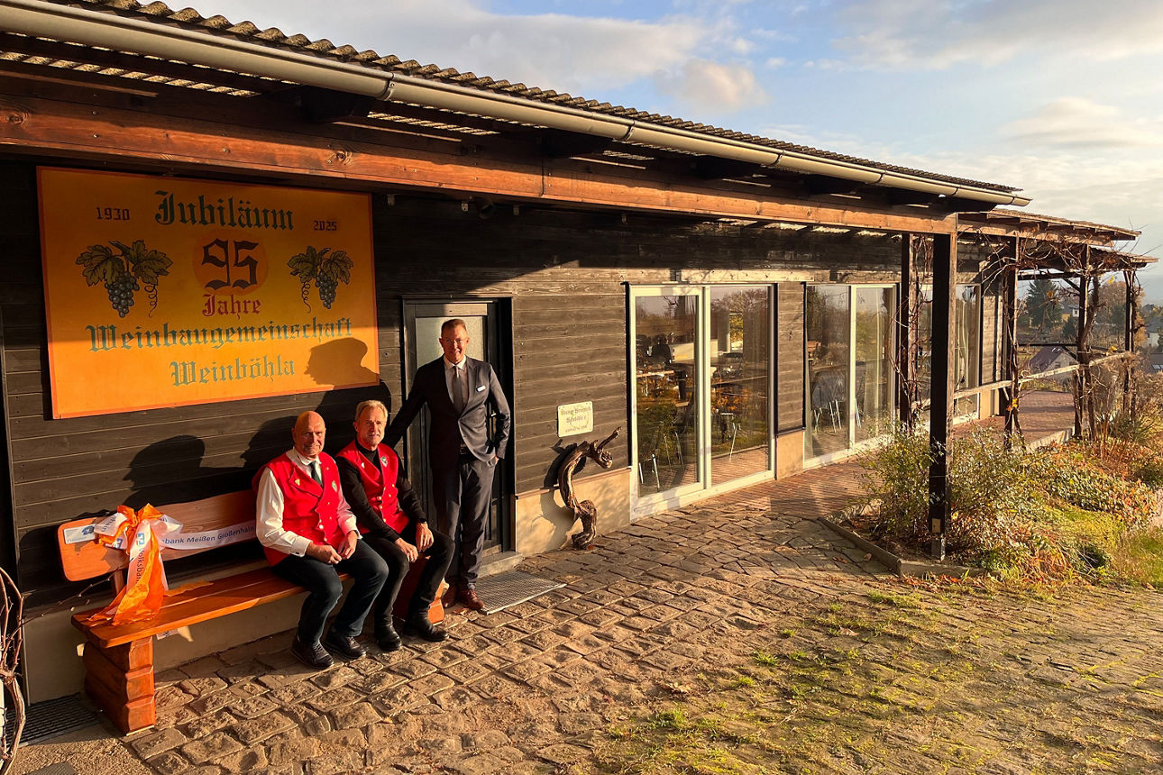 Drei Personen an einer Holzbank unter einem Vordach der Walhalla Weinböhla