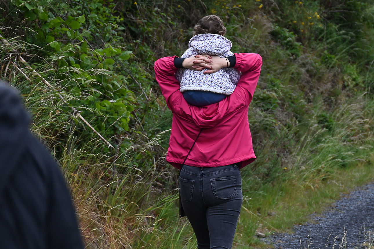 Eine junge Frau mit pinker Regenjacke trägt ein Mädchen mit geblümter Regenjacke auf den Schultern