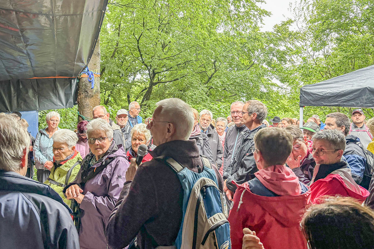Ein Mann mit grauen Haaren spricht in ein Mikrofon, er steht vor einer großen Gruppe Menschen