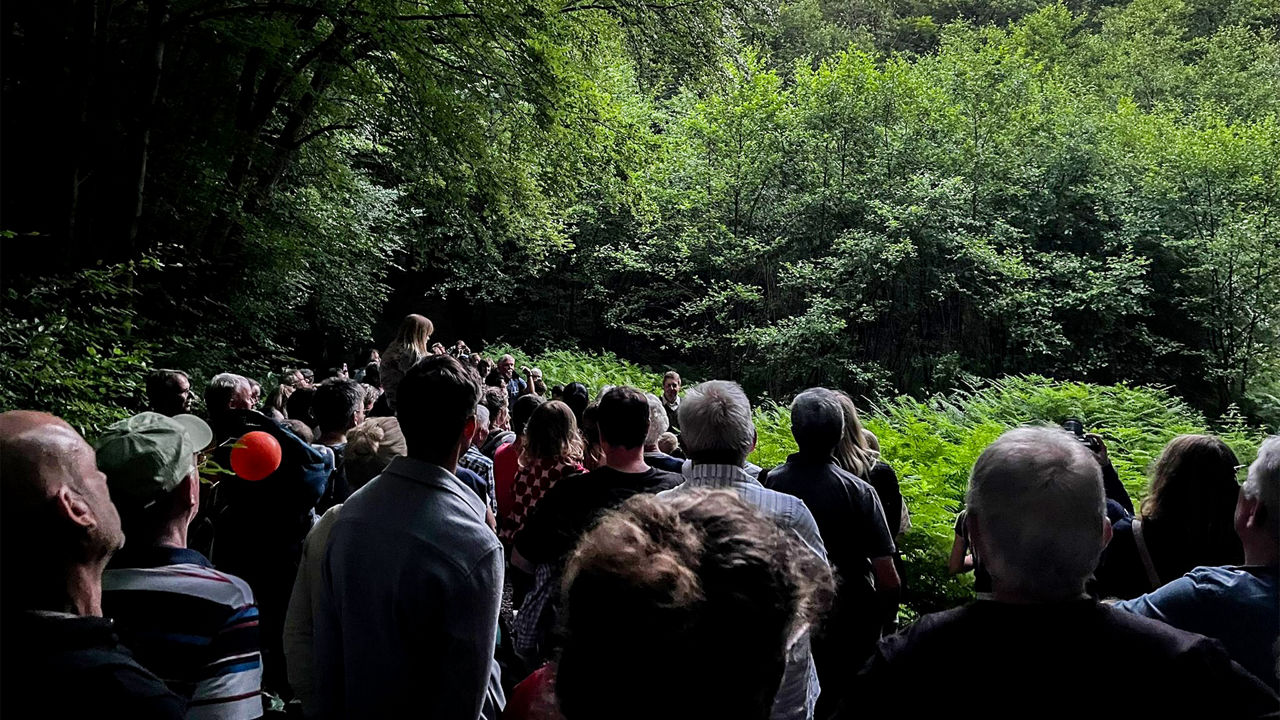Eine große Gruppe Menschen steht bei Dämmerung auf dem Wanderweg an einer Lichtung.