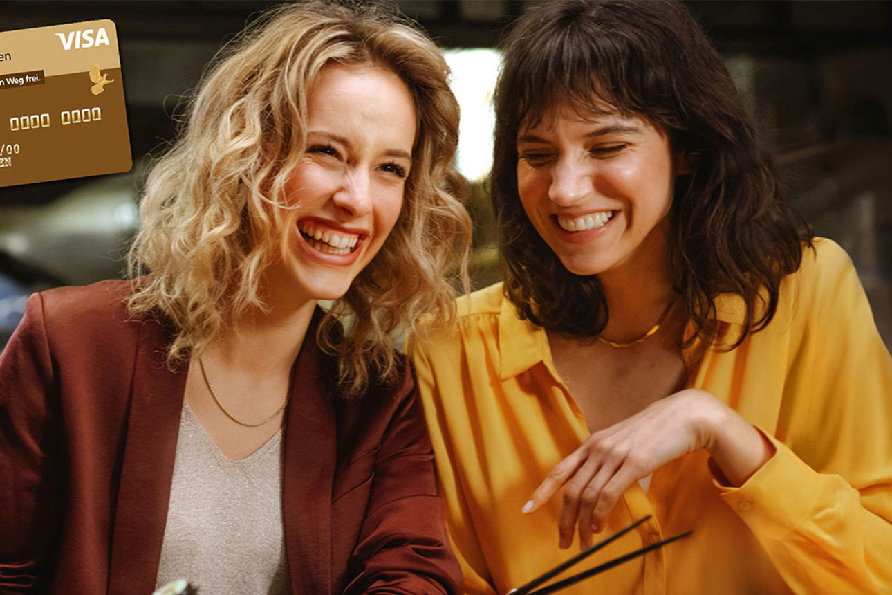 Zwei lachende Frauen sitzen im Restaurant im Bild ist eine VISA Goldcard eingeblendet