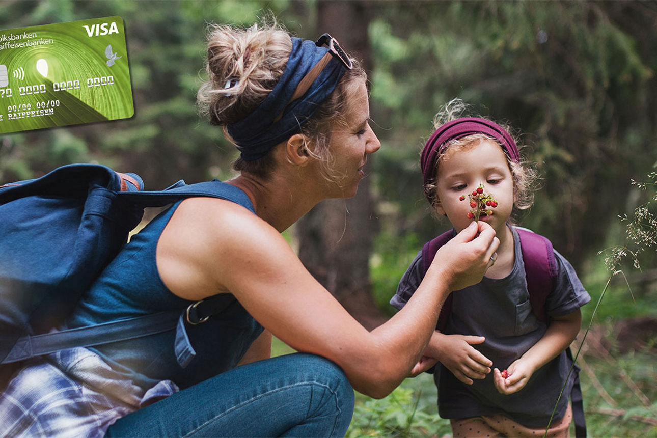 Frau mit Rucksack zeigt ihrem kleinen Kind ein Blatt im Wald