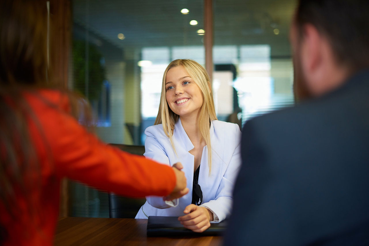 Junge Frau im Gespräch, lächelt freundlich und gibt einer anderen Person die Hand in einem modernen Büro.