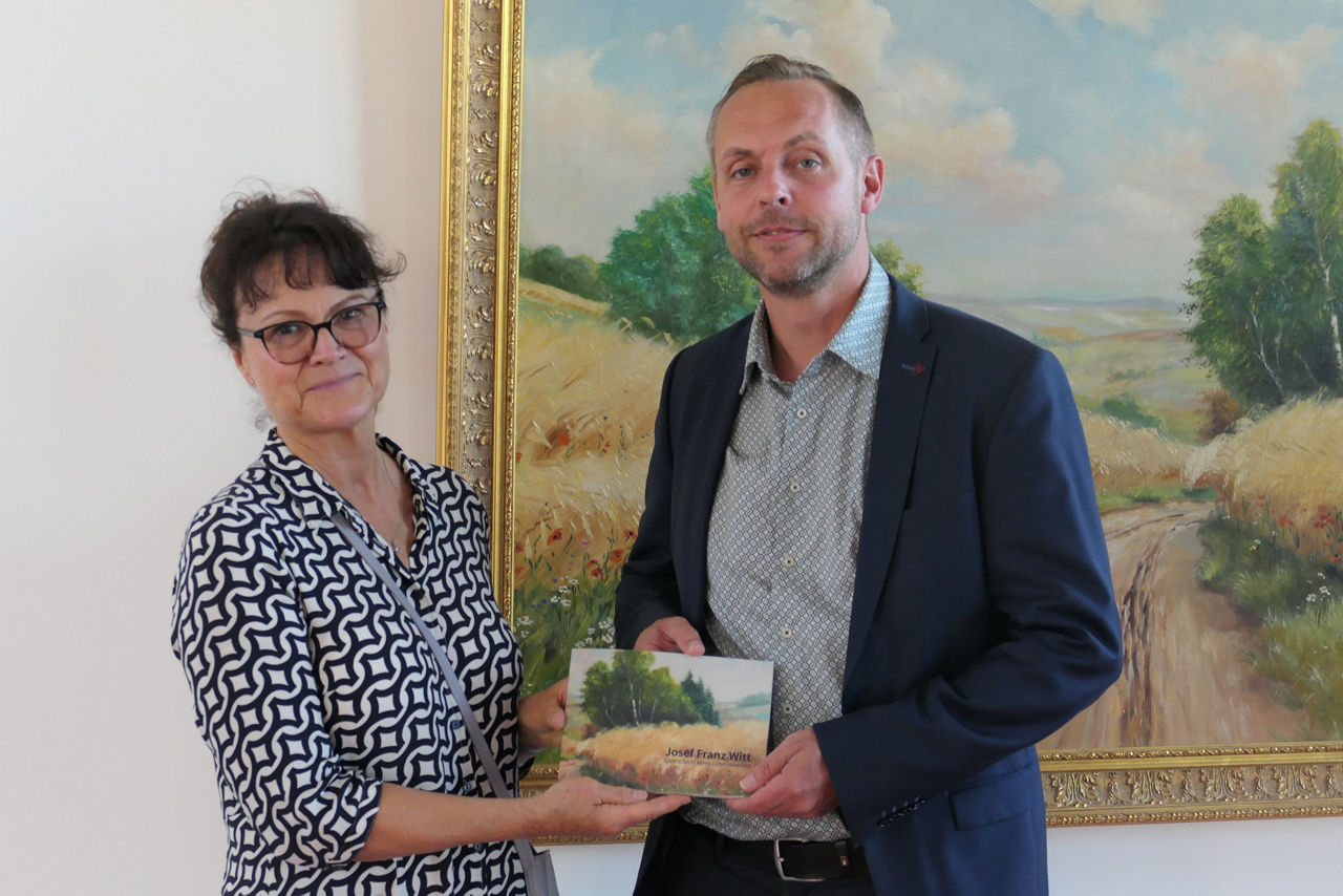 Eine Frau und ein Mann stehen vor einem Gemälde mit einer Broschüre in der Hand