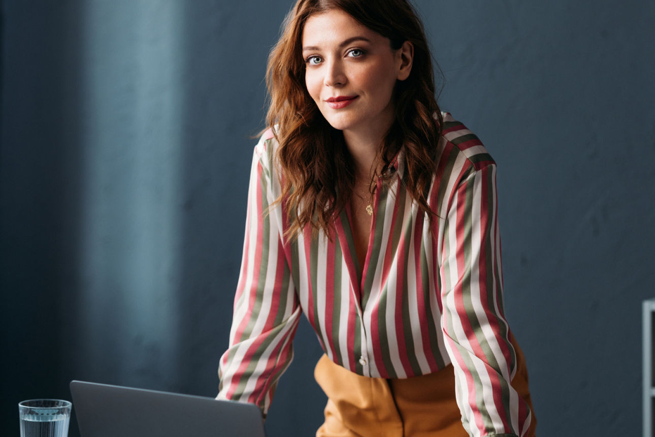 Junge Frau stützt Hände auf Schreibtisch und lächelt in die Kamera