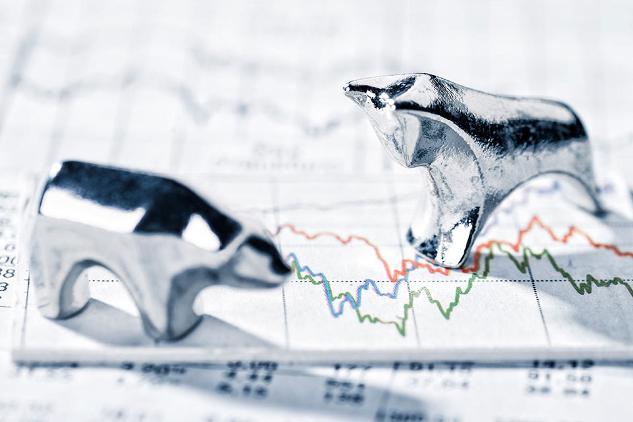 Bulle und Bär stehen auf auf einem Papier mit Börsenkursen und Zahlen