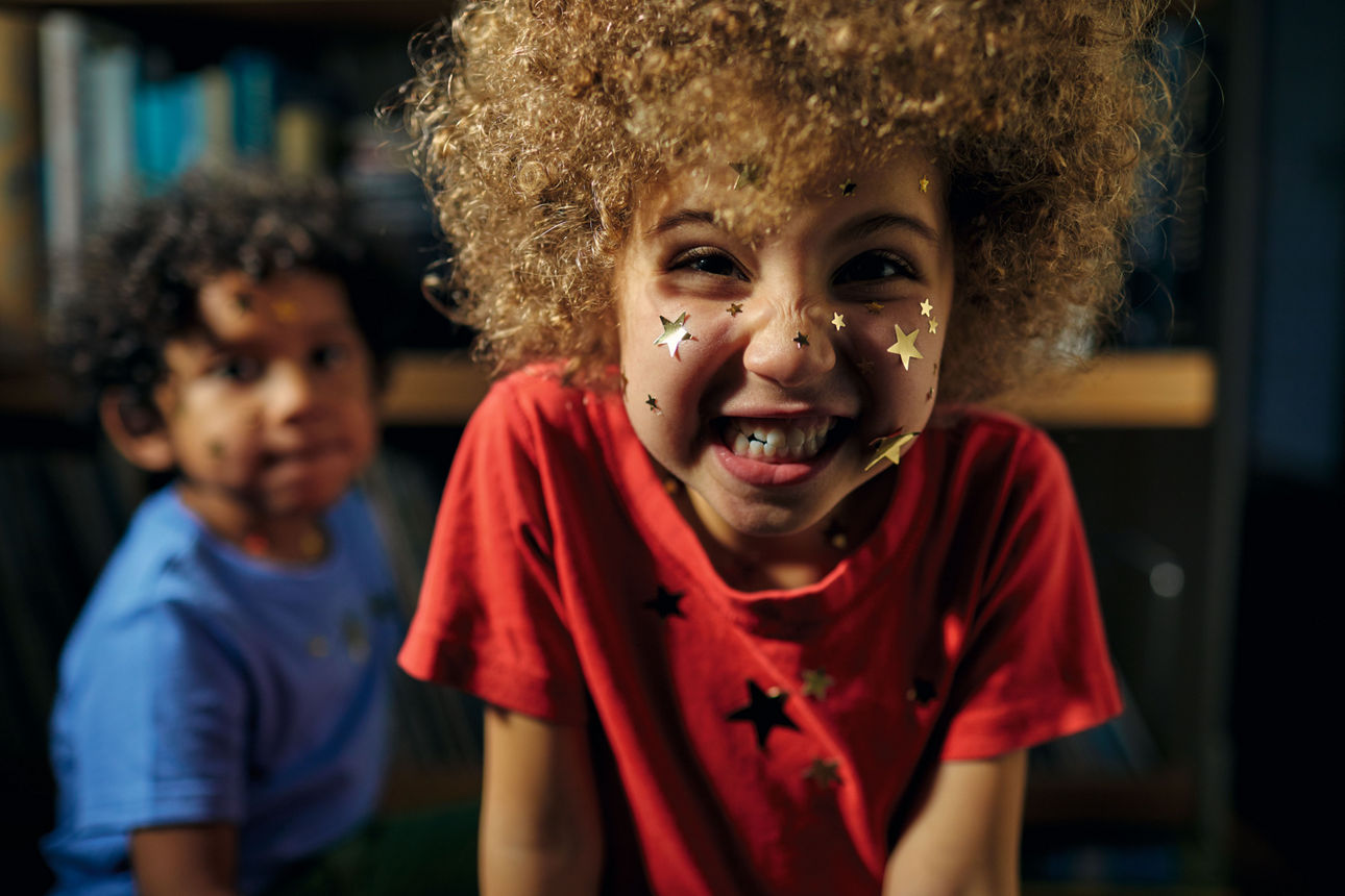 Kleines Mädchen mit einem Lockenkopf grinst in die Kamera und hat das Gesicht voller Sticker