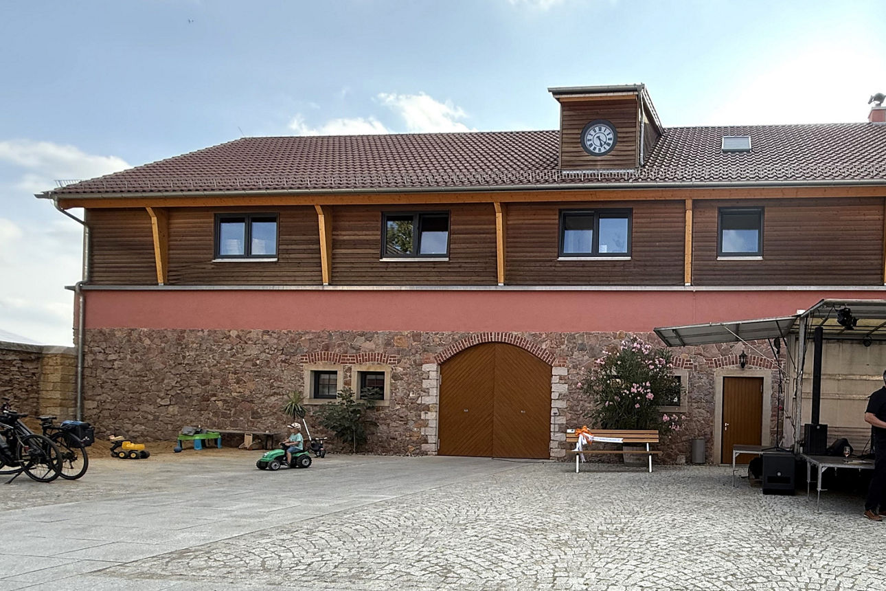 Bild von der Weinkellerei Strasser. Vor dem Eingangsbereich steht eine Holzbank mit Schleife.