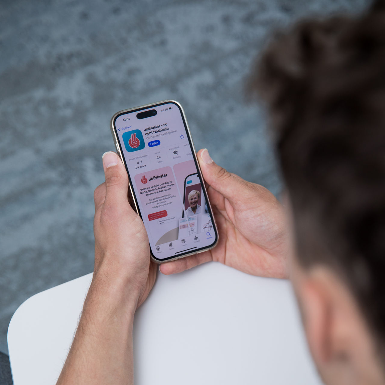 Eine Person im Anzug zeigt einer anderen Person auf einem Smartphone eine geöffnete App mit einer grafischen Darstellung.