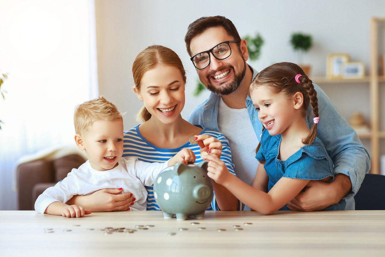 Eine glückliche Familie mit Mutter, Vater und zwei Kindern mit einem Sparschwein zu Hause.