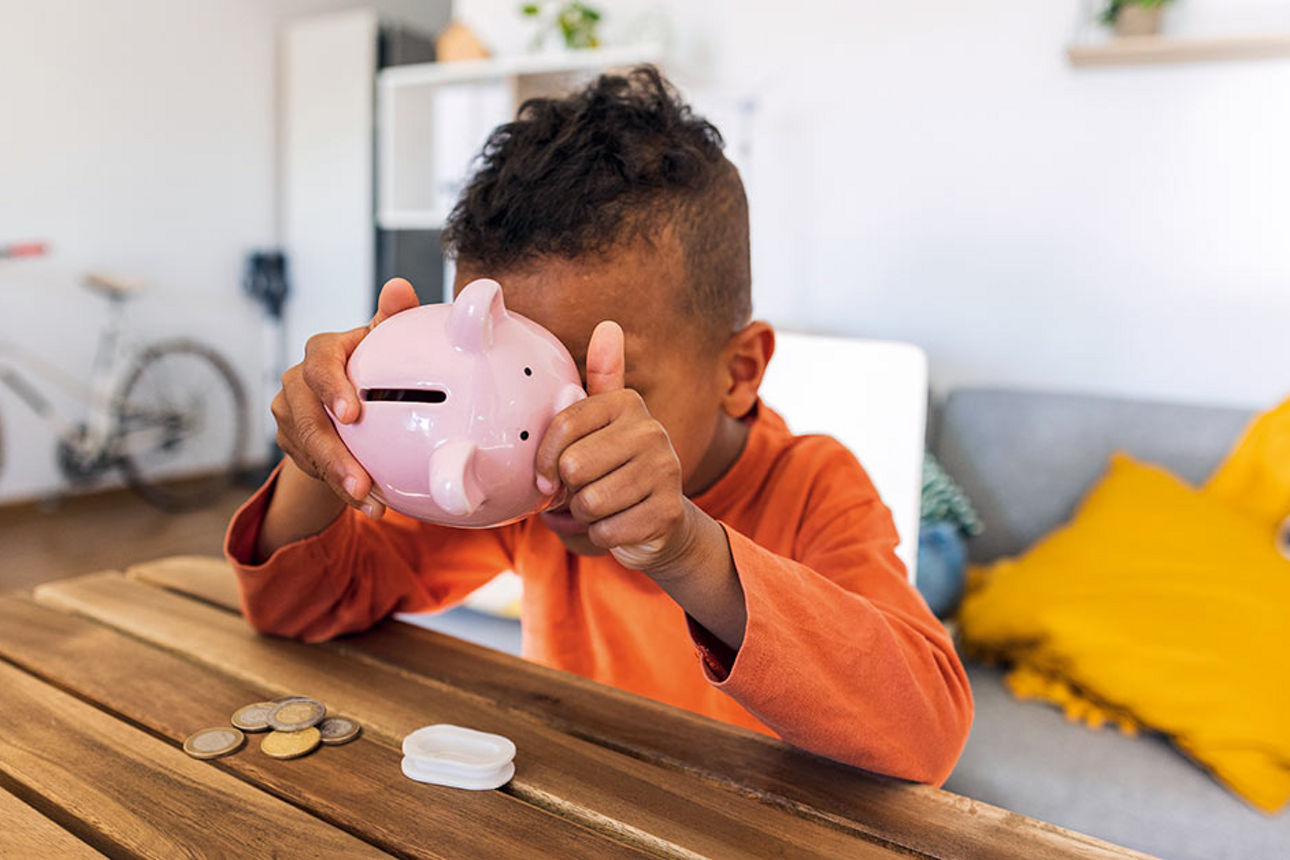 Kind sitzt mit Sparschwein am Tisch