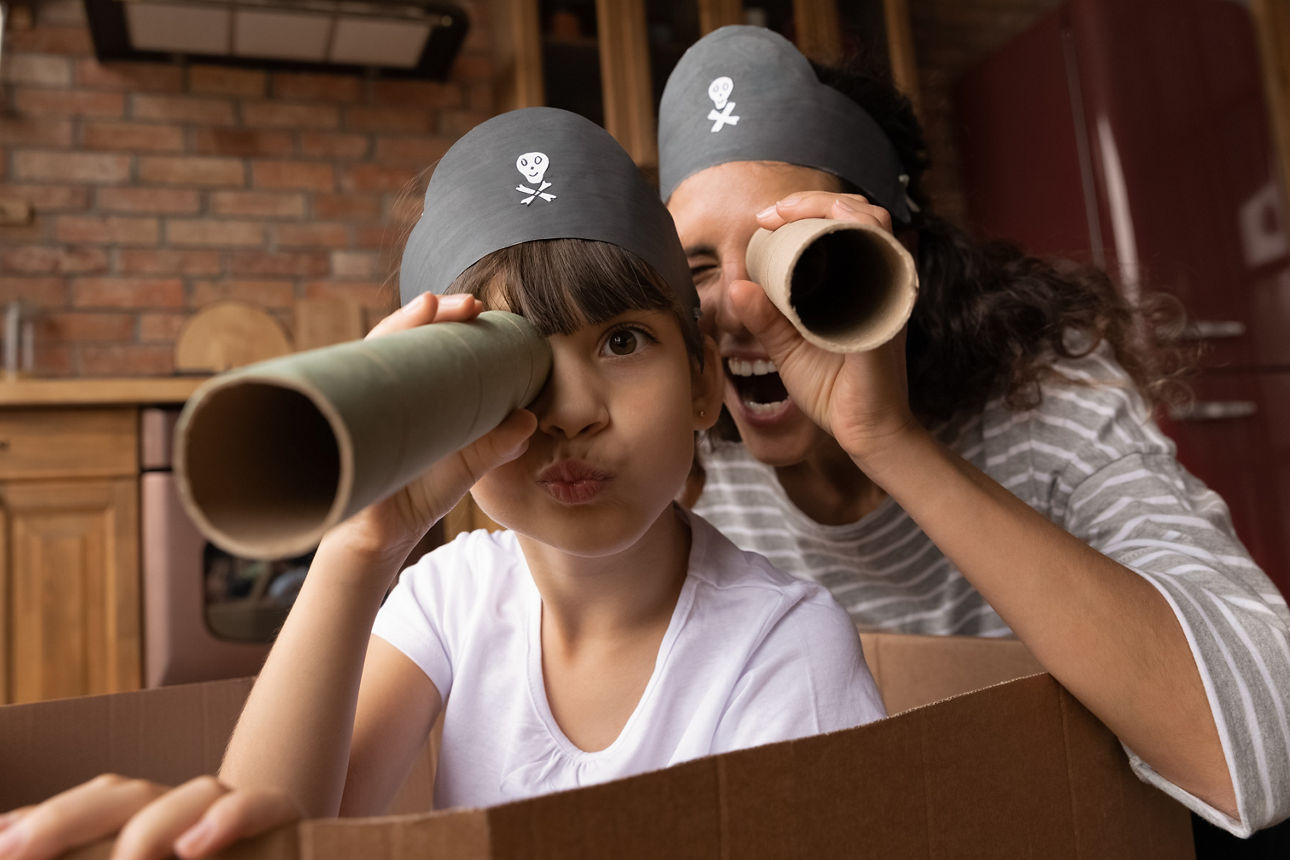 Head shot portrait happy mother and little daughter playing pirates, looking at camera, excited mum and preschool gild child wearing handmade costumes, holding paper tubes as spyglass, having fun