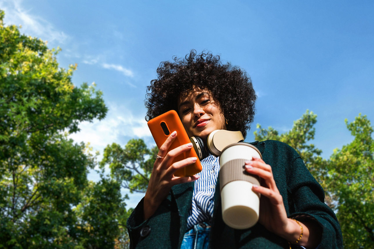 Blick von unten auf eine Frau mit Smartphone und Kaffee in den Händen
