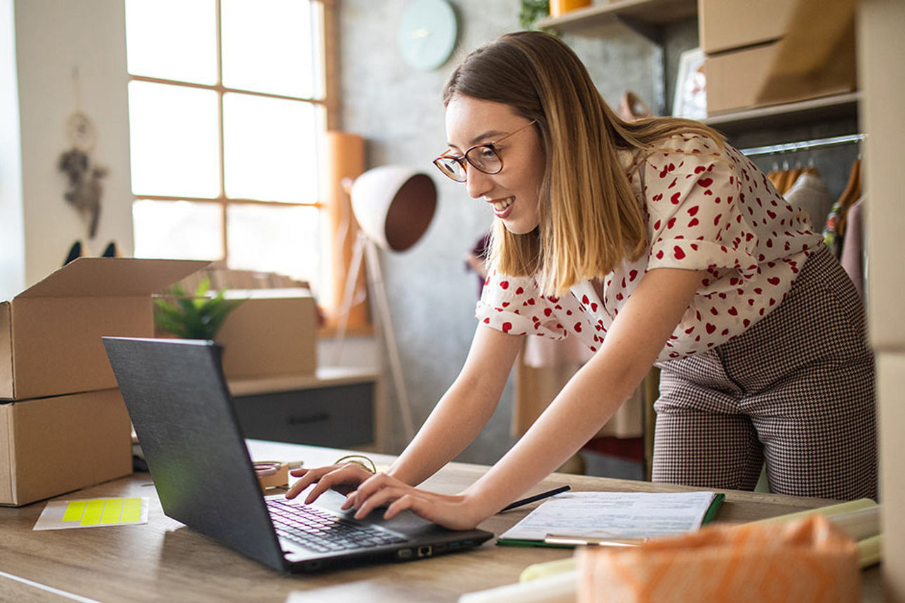 Blonde Frau am Schreibtisch stehend mit aufgeklapptem Laptop