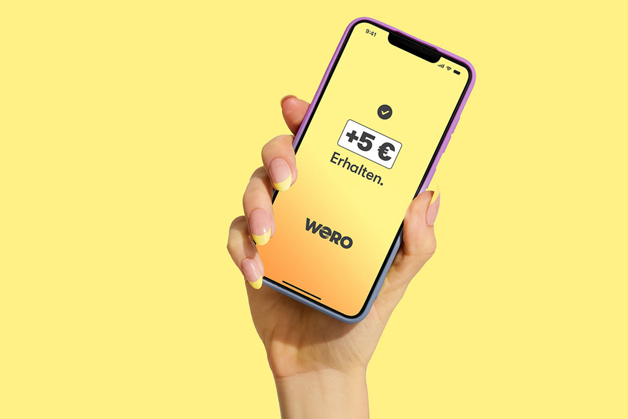 Weibliche Hand hält Smartphone mit wero-App und den Hinweis: + 5 Euro