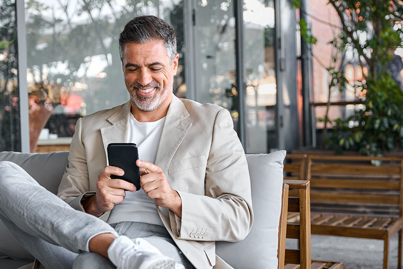 Mann sitzt mit seinem Handy auf der Bank