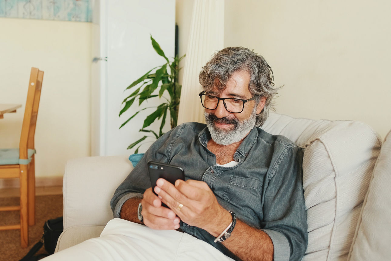 Ein Mann mittleren Alters entspannt sich zu Hause auf seiner Couch und nutzt sein Smartphone, um Textnachrichten zu schreiben.