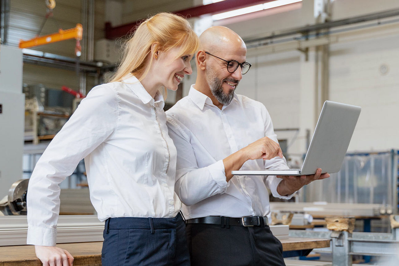 Ein Mann und eine Frau schauen in einer Fabrik gemeinsam auf einen Laptop