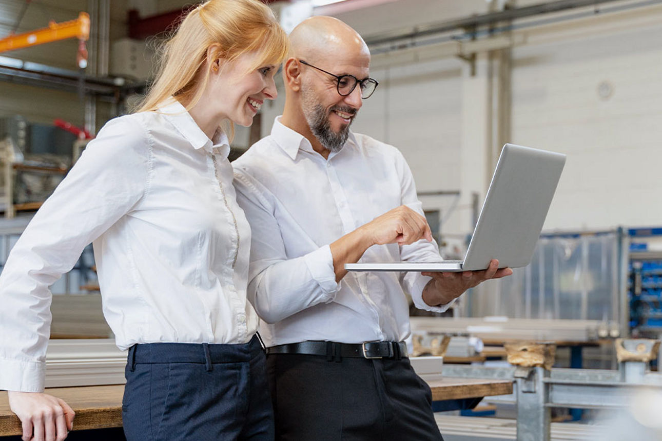 Eine Frau und ein Mann in einer Werkstatt schauen auf ein Notebook.