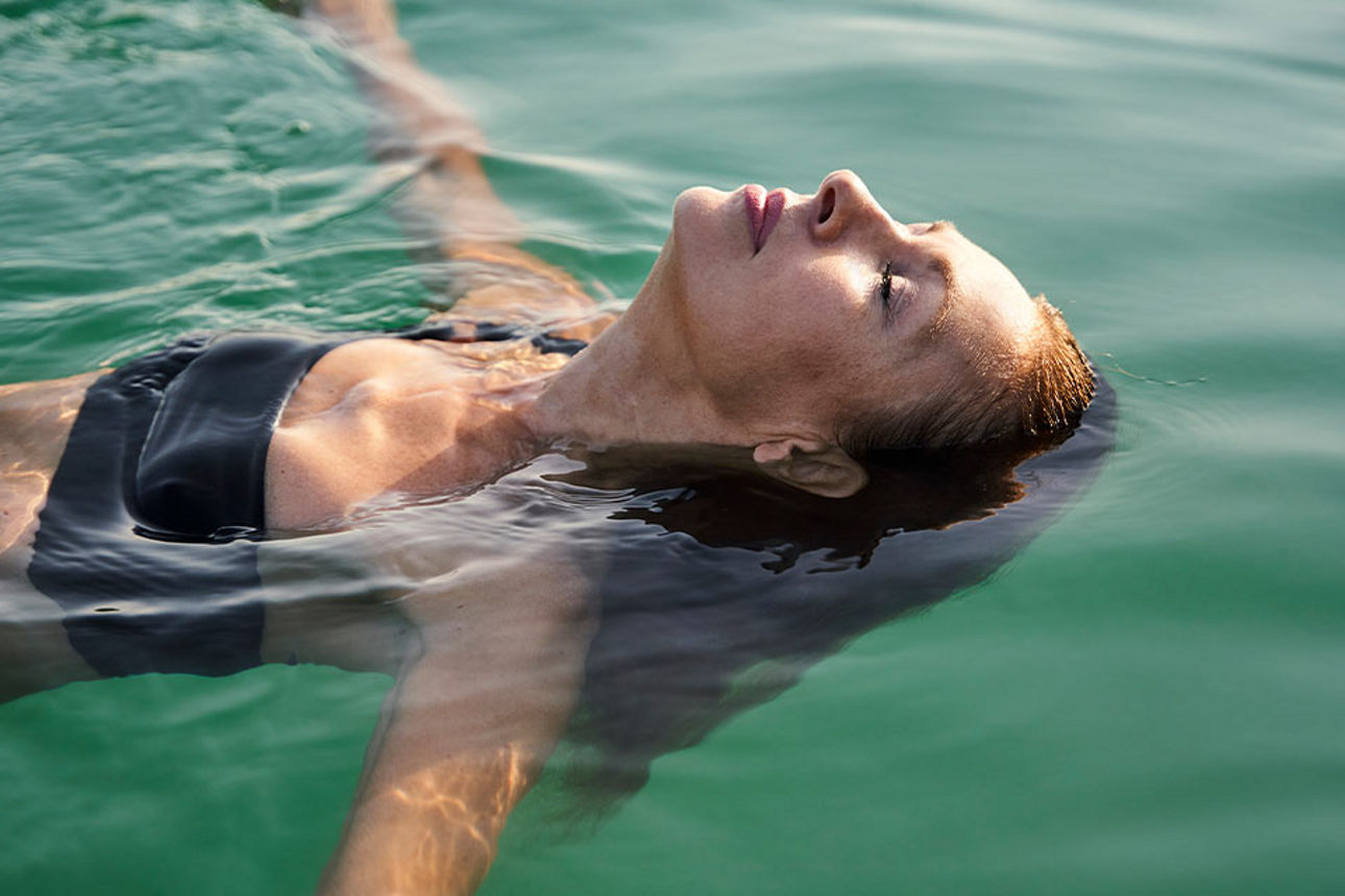 Frau liegt entspannt auf dem Rücken und schwebt im Wasser mit geschlossenen Augen