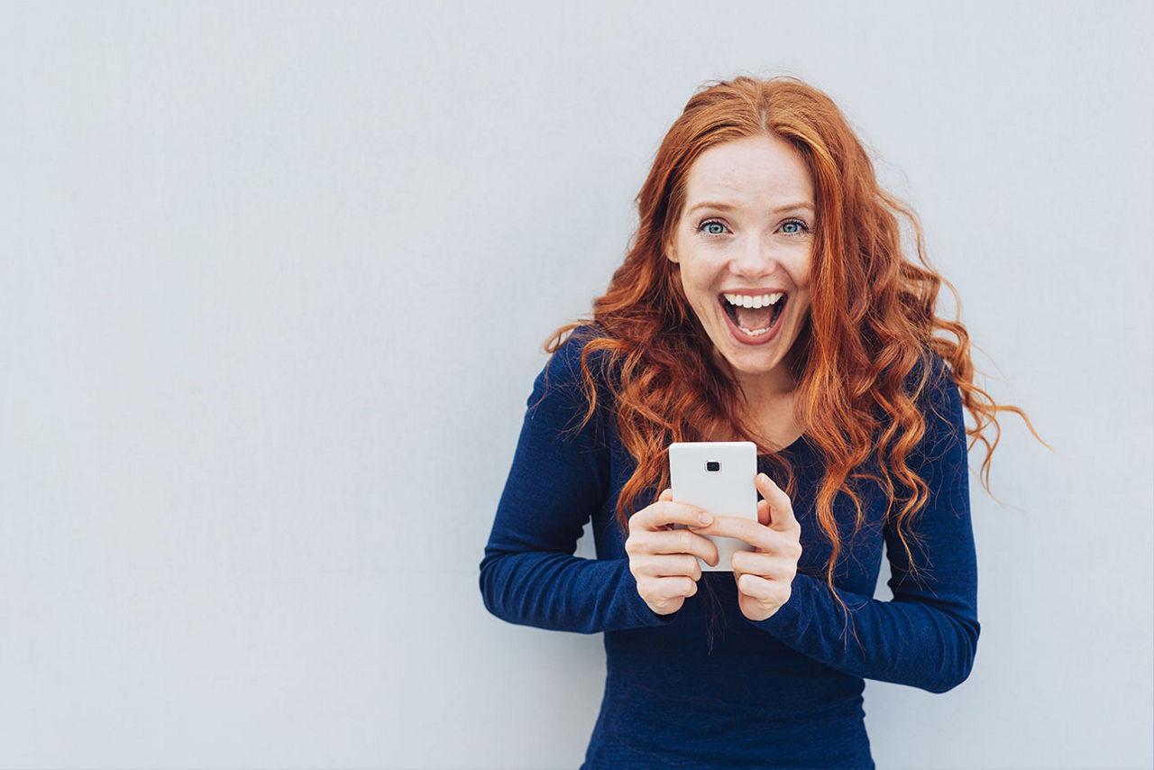 Junge rothaarige Frau lacht mit Handy in der Hand