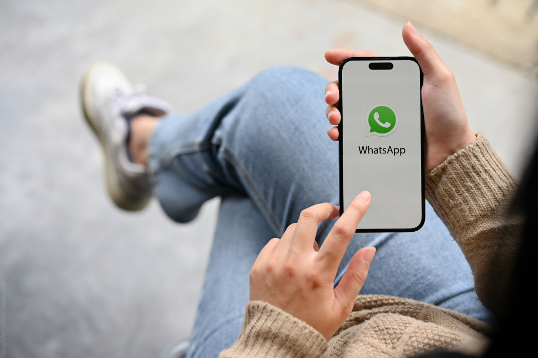 Eine Frau hält ein Smartphone in der Hand und tippt mit dem Finger auf den WhatsApp Bildschirm.