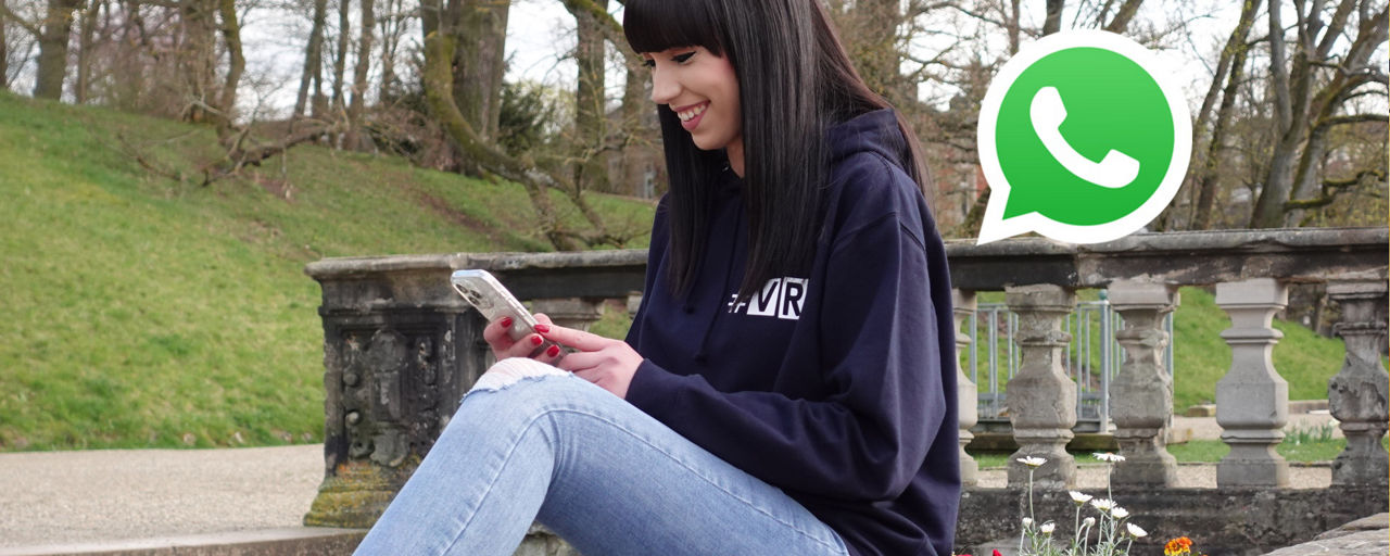 Eine junge Frau sitzt mit dem Smartphone auf einer Ballustrade