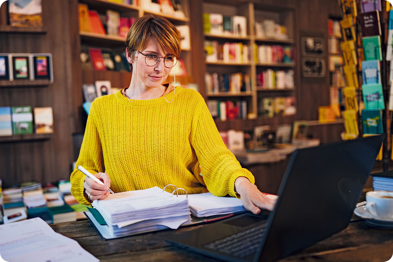 Frau sitzt an einem Tisch, vor sich ein offener Ordner und ein Laptop
