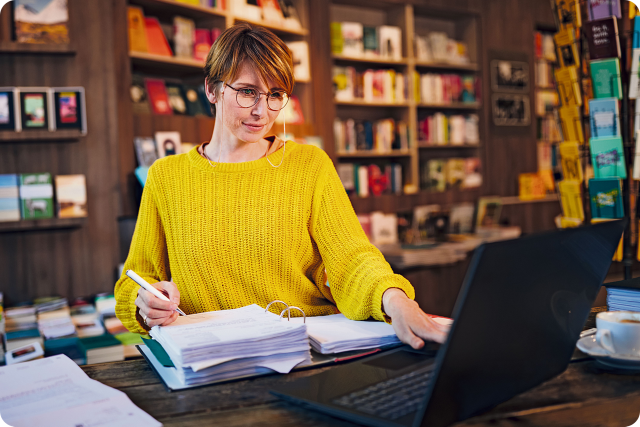 Frau sitzt an einem Tisch, vor sich ein offener Ordner und ein Laptop