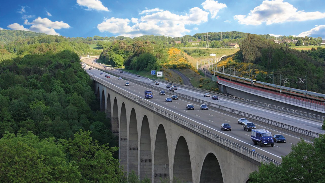 Bild der Autobahnbrücke bei Neustadt (Wied) mit ihren Rundbögen, umgeben von Wald. Nebenher führt die ICE-Trasse.