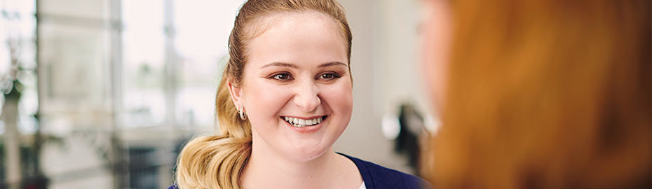 Eine Frau mit blondem Haar, das zu einem Pferdeschwanz hochgesteckt ist, lächelt warmherzig