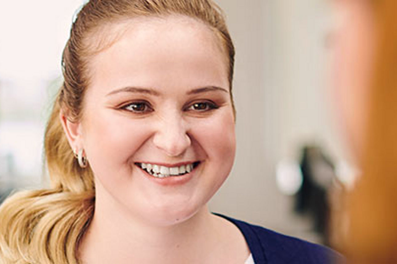 Eine Frau mit blondem Haar, das zu einem Pferdeschwanz hochgesteckt ist, lächelt warmherzig