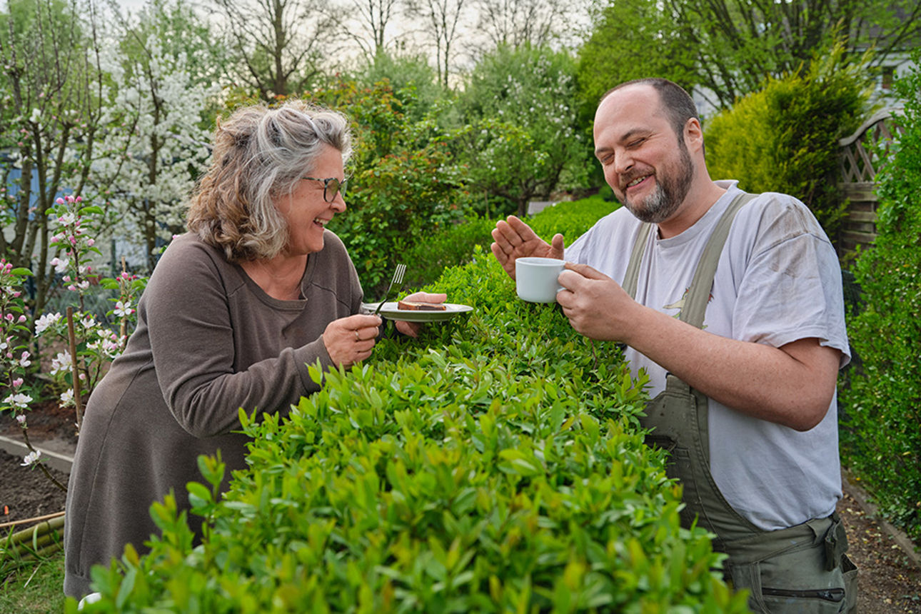 zwei Nachbarn unterhalten sich über die Hecke