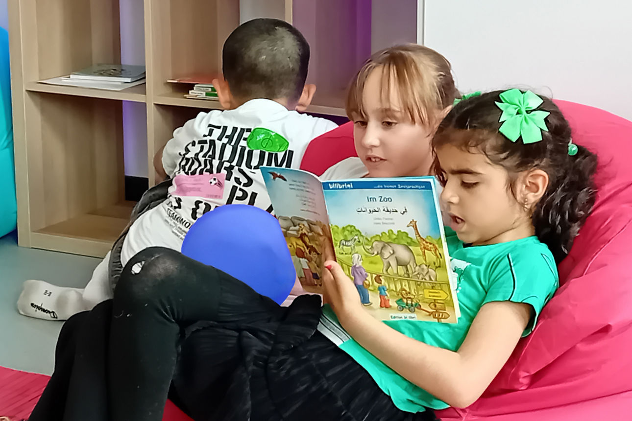 Kinder lesen gemeinsam ein Bilderbuch in einer gemütlichen Leseecke.