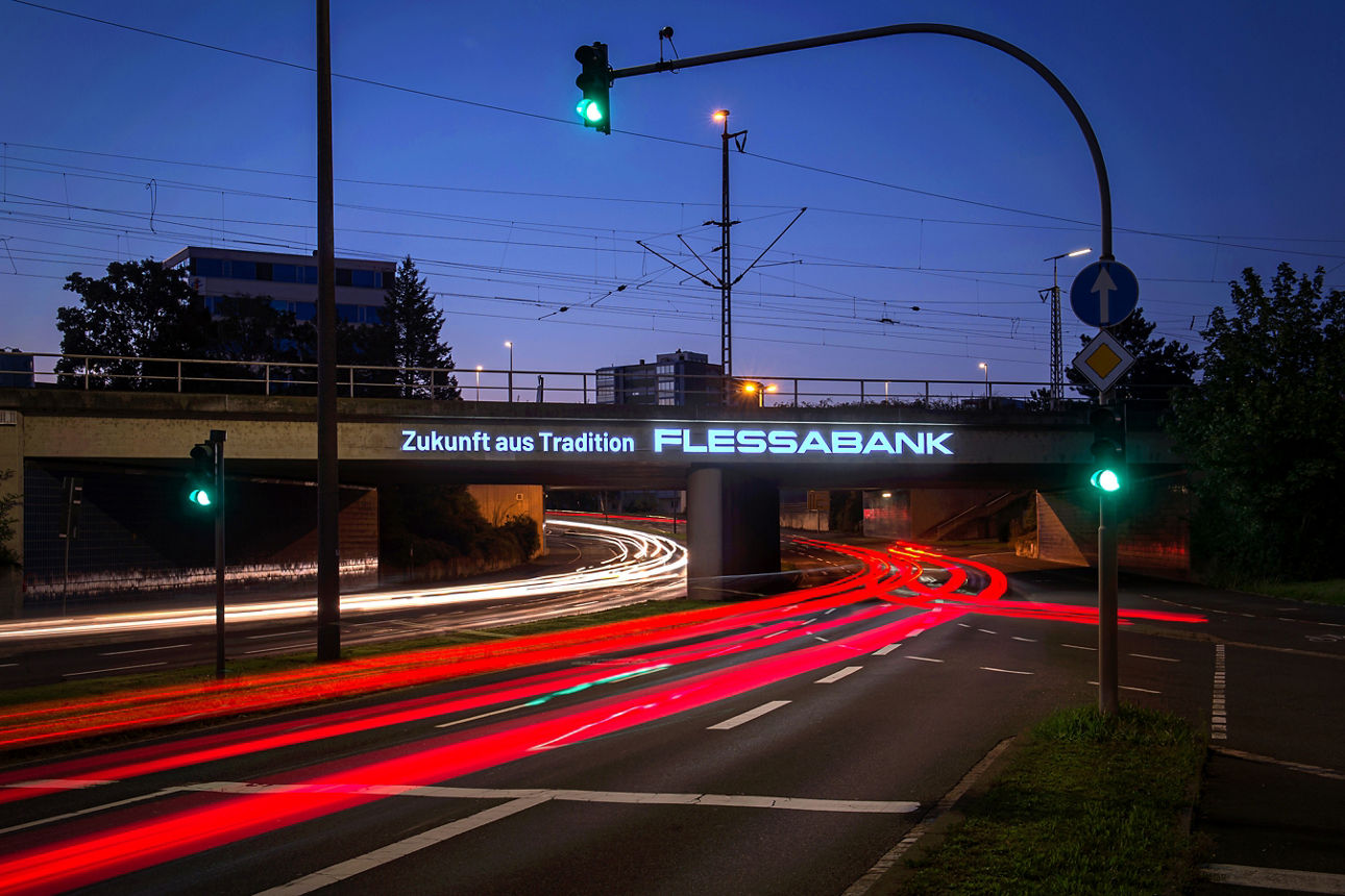 Nachtbild mit beleuchtetem Reklameschild auf der Brücke mit dem Titel: Zukunft aus Tradition Flessabank
