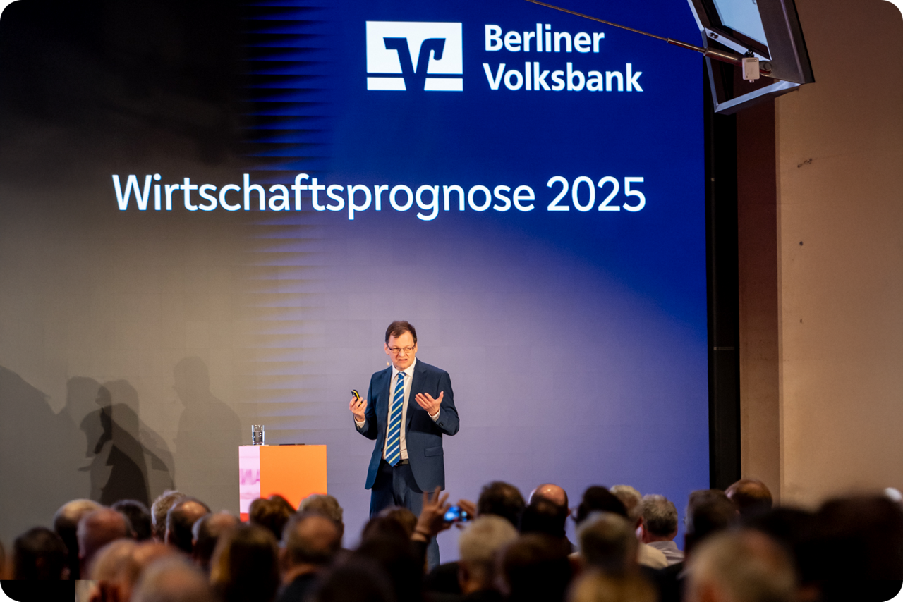 Dr. Michael Holstein steht auf einer Bühne und referiert vor Publikum