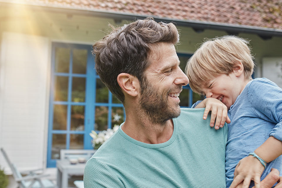 Vater und Sohn stehen lachend vor einem Haus
