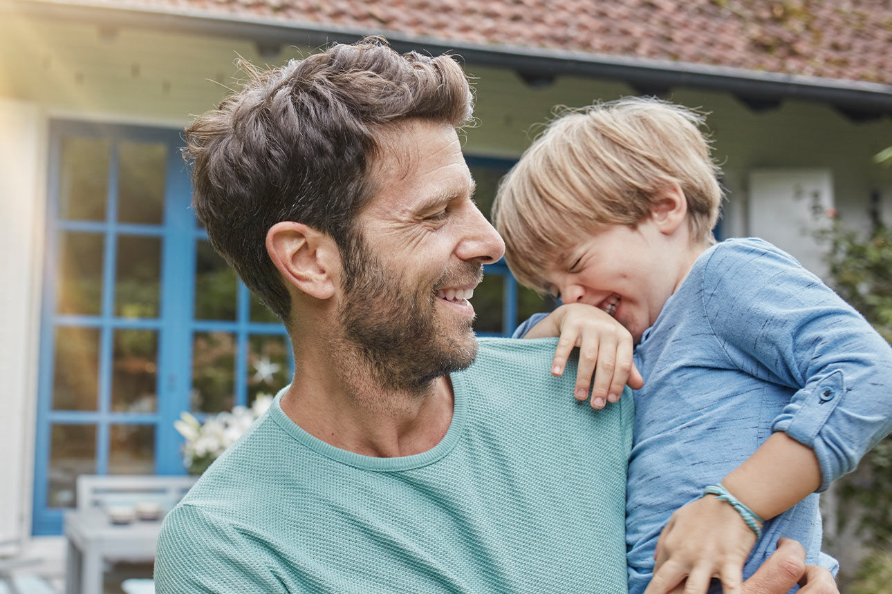 Vater und Sohn stehen lachend vor einem Haus