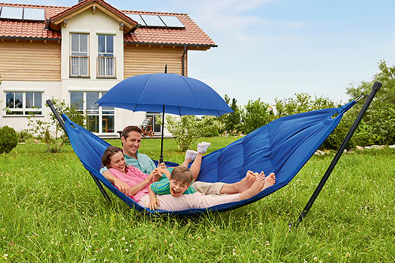 Vater, Mutter und Kind in einer Hängematte im Garten, Vater hält einen Schirm