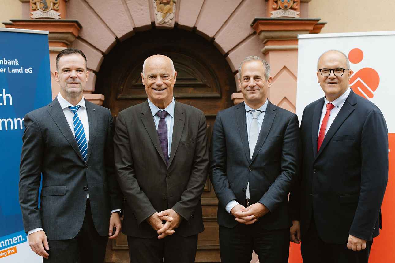 Vier Männer im Anzug stehen vor einem Gebäude