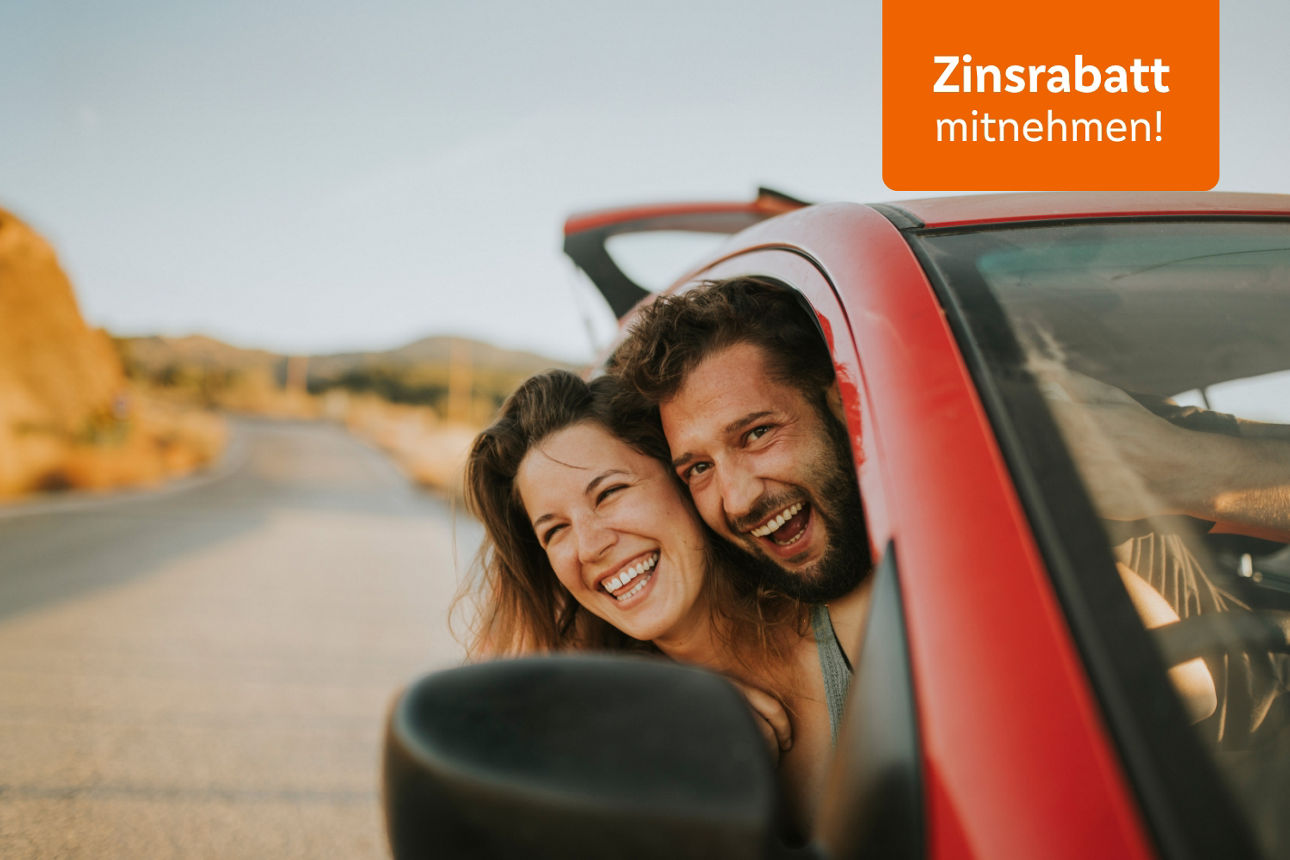 Ein fröhliches Paar lehnt sich aus einem roten Auto auf einer sonnigen Straße und lacht.