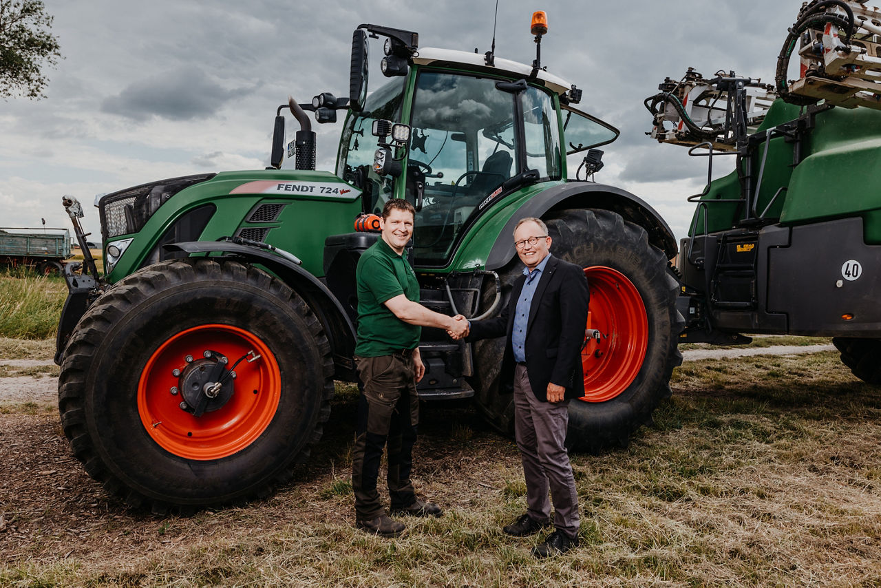 2 Männer schütteln sich vor einem Traktor die Hände