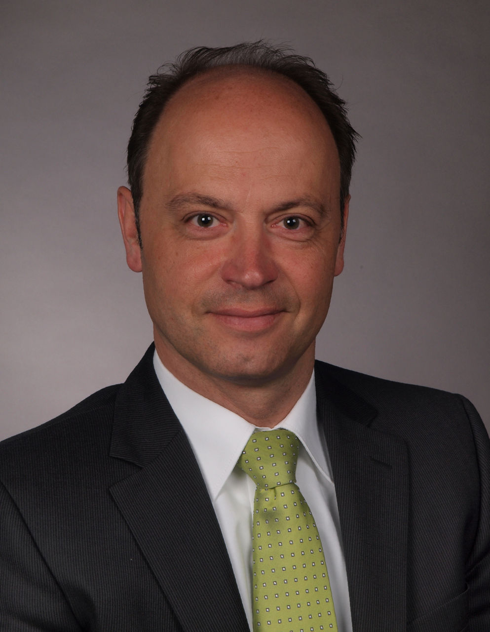 Mitarbeiter der Bank im Anzug mit grüner Krawatte lächelt in die Kamera.