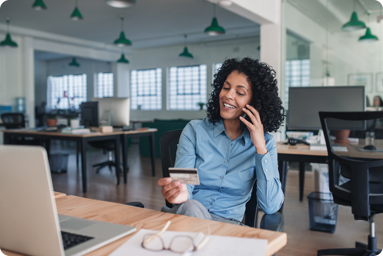 Ein Frau sitzt am Schreibtisch mit ihrer Kreditkarte und telefoniert